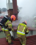 Dwóch strażaków odrywających blachę z dymiącego dachu