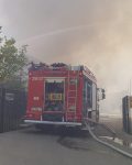 Wóz strażacki stoi w bramie, przed nim dymiący się obiekt, z wozu wychodzą węże tłoczne