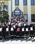Grupa strażaków pozuje do zdjęcia na zakończenie kursu podstawowego, dyplomy w dłoniach