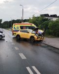 Samochód osobowy z uszkodzonym przodem i otwartą maską, po prawej stronie policjant i strażak, po lewej stronie radiowóz policji, policjant i strażak kierujący ruchem, za samochodem karetka pogotowia.