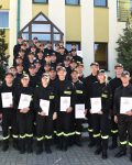 Grupa strażaków pozuje do zdjęcia na zakończenie kursu podstawowego z dyplomami w dłoniach, po lewej kierownik kursu