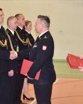 Komendant Szkoły wręcza wyróżnienia strażakom w mundurach galowych, za nim Pani Strażak z wyróżnieniami
