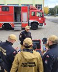 Grupa strażaków zgromadzona przed urządzeniem ACO-Streamer, za nimi znajduje się wóz strażacki