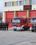 Grupa strażaków stojąca na baczność w dwuszeregu, obok dwóch wozów strażackich przed garażem bojowym JRG, dnia 11.11.2023 o godzine dwunastej.