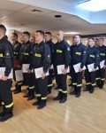 Grupa strażaków stojąca na baczność z dyplomami w dłoniach