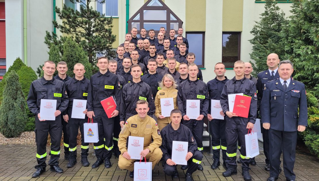 Grupa strażaków pozujących do zdjęcia na zakończenia kursu podstawowego, po prawej stronie Komendant Szkoły i kierownik kursu w mundurach galowych.