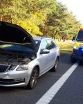 Na poboczu samochód z otwarta maską, za nim karetka pogotowia, za karetką strażak i cywil