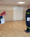 Komendant szkoły odczytuje dyplom, przed nim strażak stojący na baczność