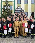 Grupa strażaków pozuje do zdjęcia na zakończenie kursu, wraz z komendantem po środku, oraz szefem kursu po lewej stronie.