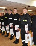 Strażacy stoją na baczność w dłoniach dyplomy oraz torby z logiem Szkoły Podoficerskiej