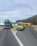 Na jezdni dwa auta ciężarowe po kolizji. Po prawej stronie stoją dwie karetki, wóz strażacki i policyjny.
