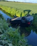 W rowie z wodą leży na dachu auto osobowe. W tle pole.