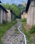 Między budynkami gospodarczymi na ścieżce brukowej leży rozwinięty wąż pożarniczy.