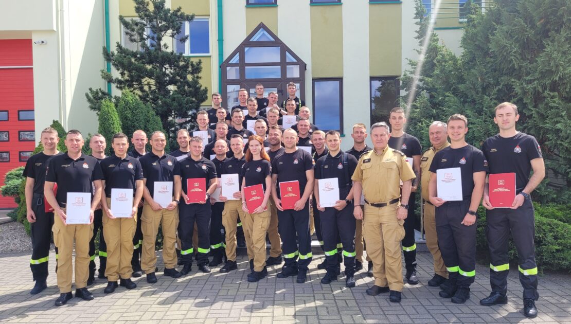 36 strażaków w mundurach koszarowych i służbowych stoją , część z nich trzyma teczki
