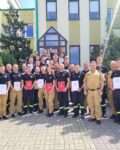 36 strażaków w mundurach koszarowych i służbowych stoją , część z nich trzyma teczki