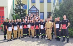 36 strażaków w mundurach koszarowych i służbowych stoją , część z nich trzyma teczki