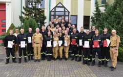 36 strażaków w mundurach koszarowych i służbowych stoją , część z nich trzyma teczki