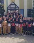 38 strażaków w mundurach koszarowych i służbowych stoją , część z nich trzyma teczki