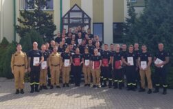 38 strażaków w mundurach koszarowych i służbowych stoją , część z nich trzyma teczki