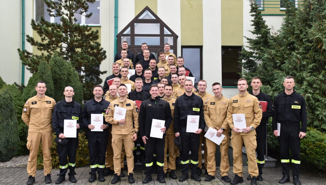 36 strażaków w mundurach koszarowych i służbowych stoją , część z nich trzyma teczki