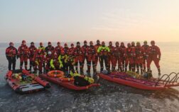 26 strażaków w specjalnych ubraniach stoją na lodzie, przed nimi leżą sanie i trapy do ratownictwa.