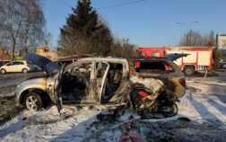 na parkingu stoi spalone auto osobowe pokryte pianą gaśniczą. W tle widać samochód strażacki
