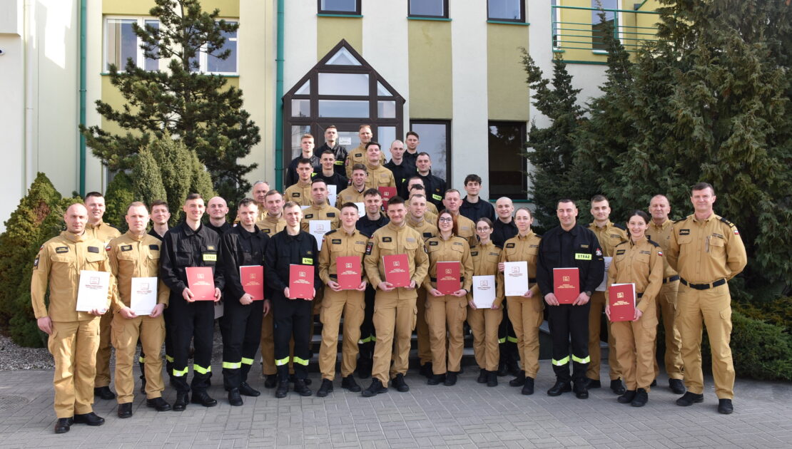 36 strażaków w mundurach koszarowych i służbowych stoją , część z nich trzyma teczki