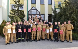 36 strażaków w mundurach koszarowych i służbowych stoją , część z nich trzyma teczki