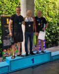 Trzech strażaków w strojach sportowych stoi na podium