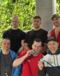 6 strażaków w strojach sportowych stoi w pomieszczeniu, dwóch z nich trzyma medale