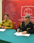 komendant szkoły podpisuje dokumenty. Przy stoliku siedzi funkcjonariuszka