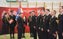 Strażacy stoją w szeregu, komendant wręcza dokumenty