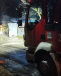 4 Po prawej stornie kabina pojazdu strażackiego przed nią w tle garaż znad którego unosi się dym