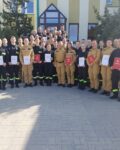 38 strażaków w mundurach koszarowych i służbowych stoją , część z nich trzyma teczki