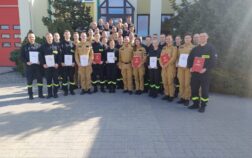 38 strażaków w mundurach koszarowych i służbowych stoją , część z nich trzyma teczki