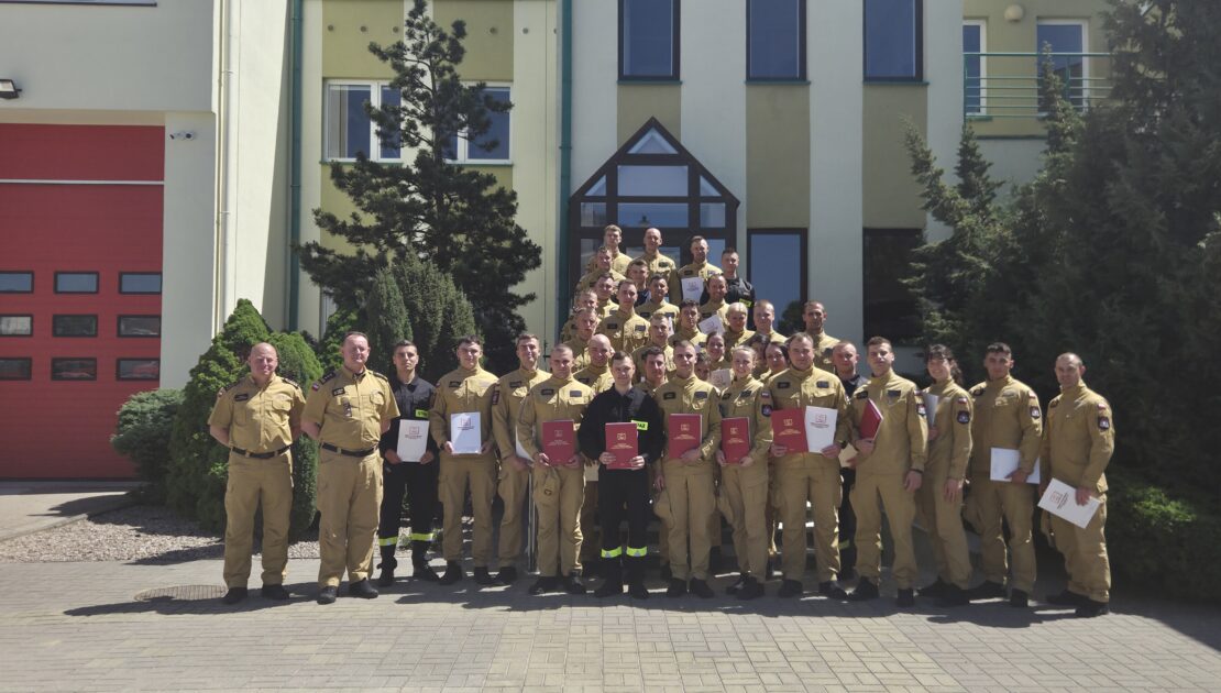 38 strażaków w mundurach koszarowych i służbowych stoją , część z nich trzyma teczki