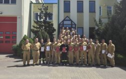 38 strażaków w mundurach koszarowych i służbowych stoją , część z nich trzyma teczki