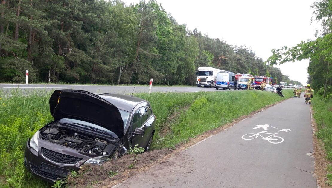 W przydrożnym rowie stoi rozbite auto, w tle droga na której stoją auta.