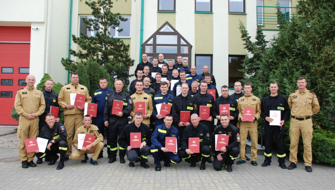 38 strażaków w mundurach koszarowych i służbowych stoją , część z nich trzyma teczki